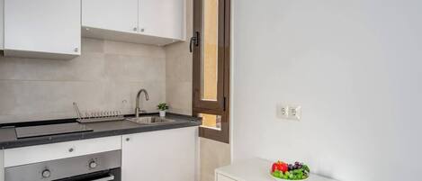 A kitchen with white cabinets, a black countertop, a stainless steel oven, a sink, and a small white cabinet with a fruit bowl.
