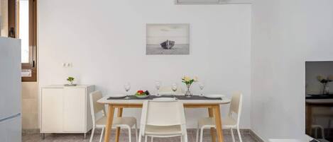 A modern dining area with a wooden table and four chairs, a white cabinet, and a small plant on the cabinet.