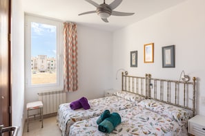 A bedroom with two beds, a window with curtains, a ceiling fan, and a view of buildings outside.