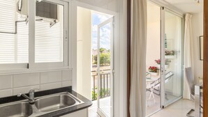 Una cocina con un lavamanos, una ventana con persianas y vistas a un balcón con mesa y sillas.
