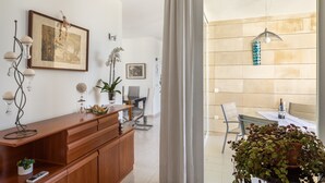 Una sala de estar moderna con un aparador de madera, una obra de arte enmarco, una planta en maceta y una zona de comedor con mesa y sillas.