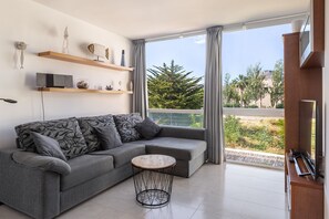 Una sala moderna con un sofá gris, una mesa de centro redonda de madera y un televisor sobre un mueble de madera.