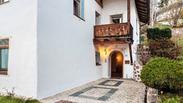 Un edificio con facciata bianca, un balcone in legno e un muro in pietra.