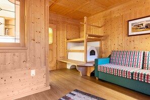 A wooden interior with bunk beds, a green sofa, and a framed picture on the wall.