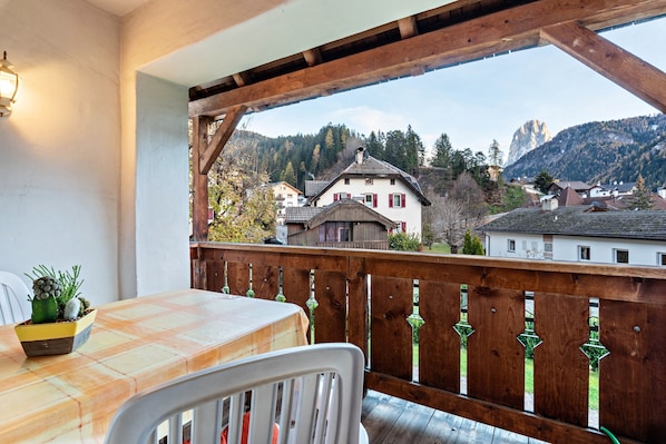 A balcony with a wooden railing, a table with a checkered tablecloth, and a potted plant.