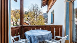 Un balcone con tavolo e sedie, ringhiere in legno e vista su case e alberi.