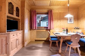 A wooden interior with a dining table, chairs, a television, and a window with curtains.