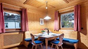 Una baita in legno con un tavolo da pranzo, sedie imbottite blu, una panca e una finestra con tende.