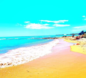 A beach with clear water, a sandy shore, and a few people.