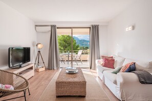 A living room with a television, wicker ottoman, and a sofa with cushions.