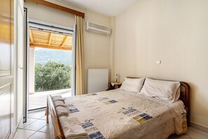 A bedroom with a bed, a window with curtains, an air conditioning unit, and a view of greenery outside.