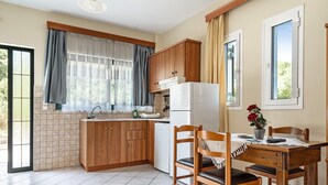 Una cuina amb armaris de fusta, un refrigerador blanc, una taula de dinar amb cadires i una finestra amb cortines.