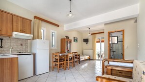 Cuina amb armaris de fusta, nevera, taula de dinar amb cadira, sofà i zona de banyera.