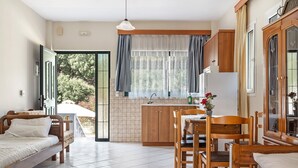 Habitació compacta amb un llit, taula de menjador, cadires, zona de cuina i una finestra gran amb cortines.