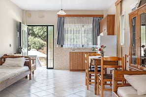 A compact room with a bed, a dining table, chairs, a kitchen area, and a large window with curtains.