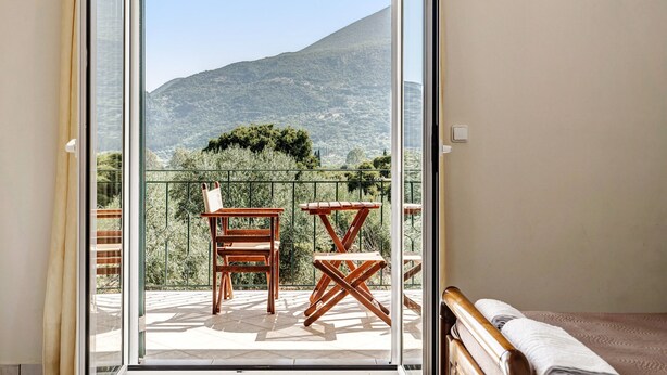 Un balcón con mesa y sillas de madera, una cama y vistas a la montaña.