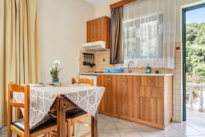 A kitchen with wooden cabinets, a tiled backsplash, a window with lace curtains, and a dining table with a patterned tablecloth.
