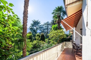 A balcony with a view of lush greenery, a palm tree, and a striped awning.