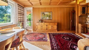 Een kamer met houten lambrisering, een eettafel, stoelen, een kast en een vloerkleed.