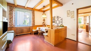 Een keuken met houten balken, een eethoek met een tafel en stoelen, een inbouwoven en een raam met gordijnen.