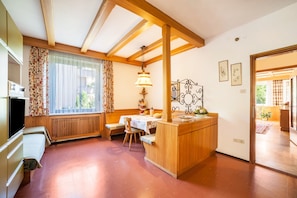A kitchen with wooden beams, a dining area with a table and chairs, a built-in oven, and a window with curtains.