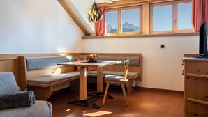 Um quarto aconchegante com um banco de madeira, uma mesa e uma cadeira, janela com vista para montanhas e teto com vigas de madeira.