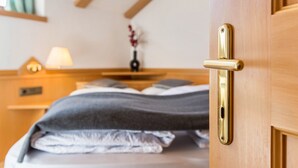 Quarto de hotel com porta de madeira, cama com almofadas, mesa de cabeceira com abajur e um vaso com flores.