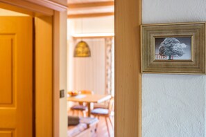 Une porte qui mène à une pièce où est accrochée, au mur, une image encadrée représentant un arbre.