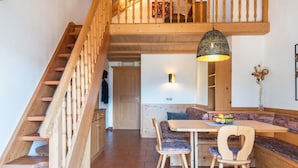 En trätrappa som leder upp till ett loft, en matplats med en bänk och ett bord samt en hänglampa.