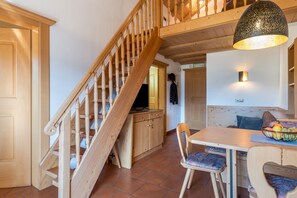 A wooden staircase leading to a loft, a dining area with a table and chairs, and a kitchen with wooden cabinets. - Apartment Häuslerhof Tilia with Mountain View, Balcony & Wi-Fi (Niederdorf)
