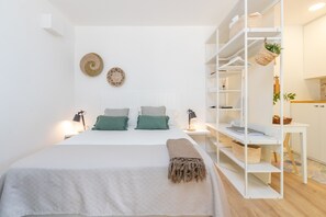 Une chambre à coucher bien rangée, avec un lit, des tables de chevet, une armoire blanche et un petit bureau doté d’étagères.