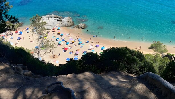 Een strand met helderblauw water, een zandstrand en talloze kleurrijke parasols.