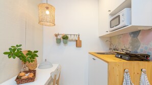 Een kleine keuken met een magnetron, een houten kastje en een ophangkraam met keukengerei.