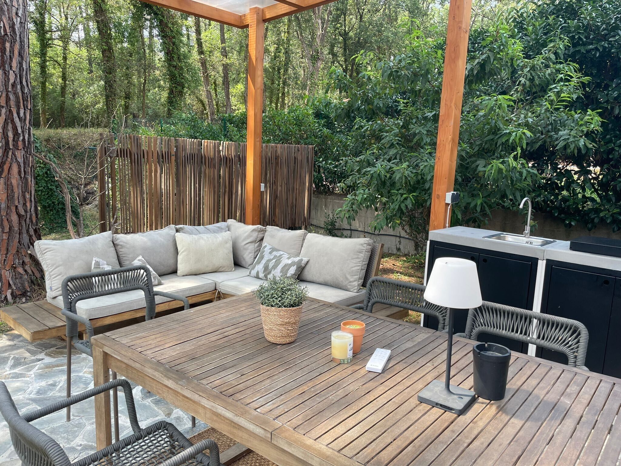 An outdoor patio with a wooden table, wicker chairs, a sofa, and a built-in grill.
