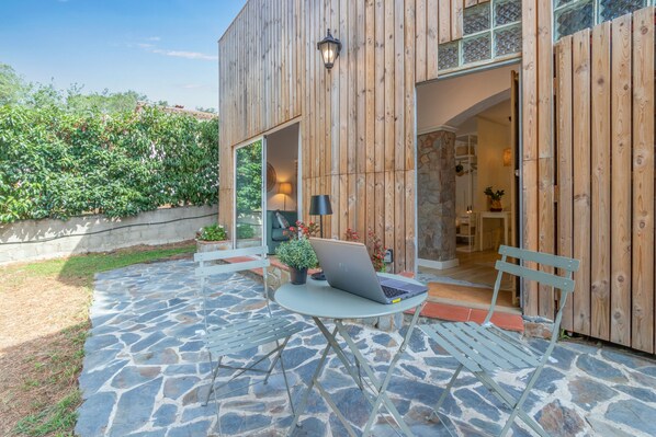 Un patio exterior moderno con suelo de piedra, una computadora portátil sobre una mesa y un banco.