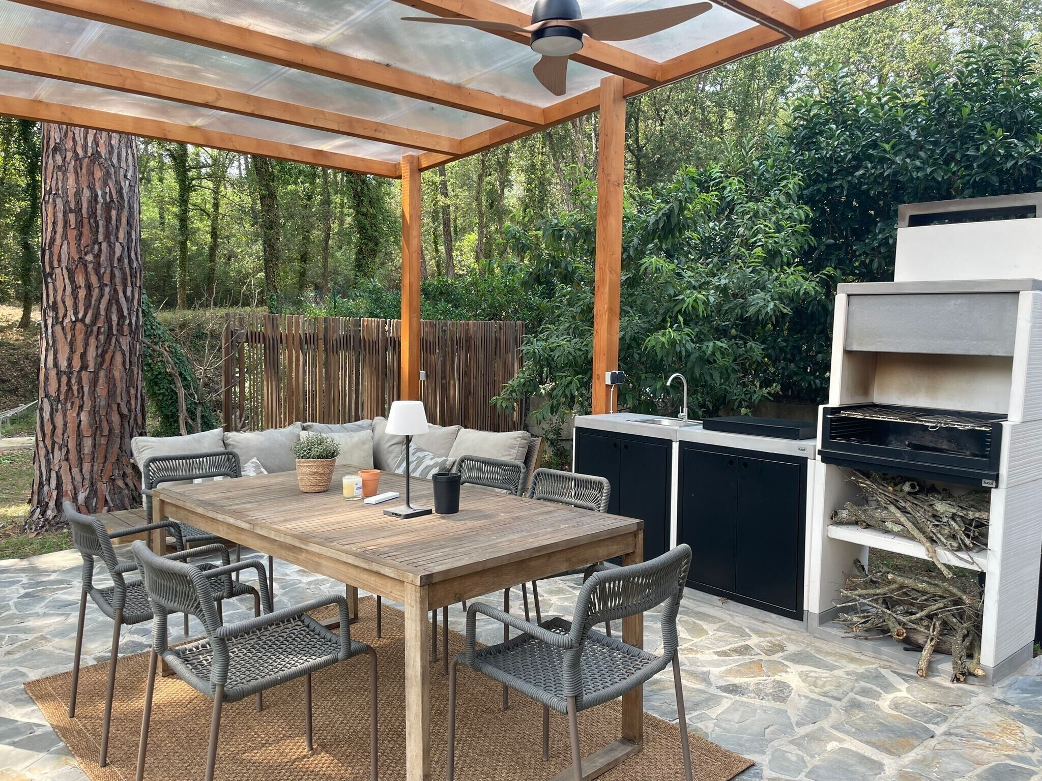 Un patio exterior con mesa y sillas de madera, una parrilla y una pérgola.