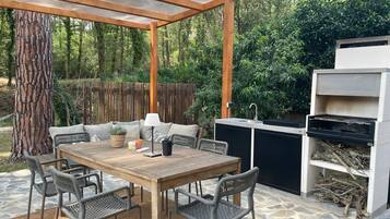 Un patio exterior con mesa y sillas de madera, una parrilla y una pérgola.