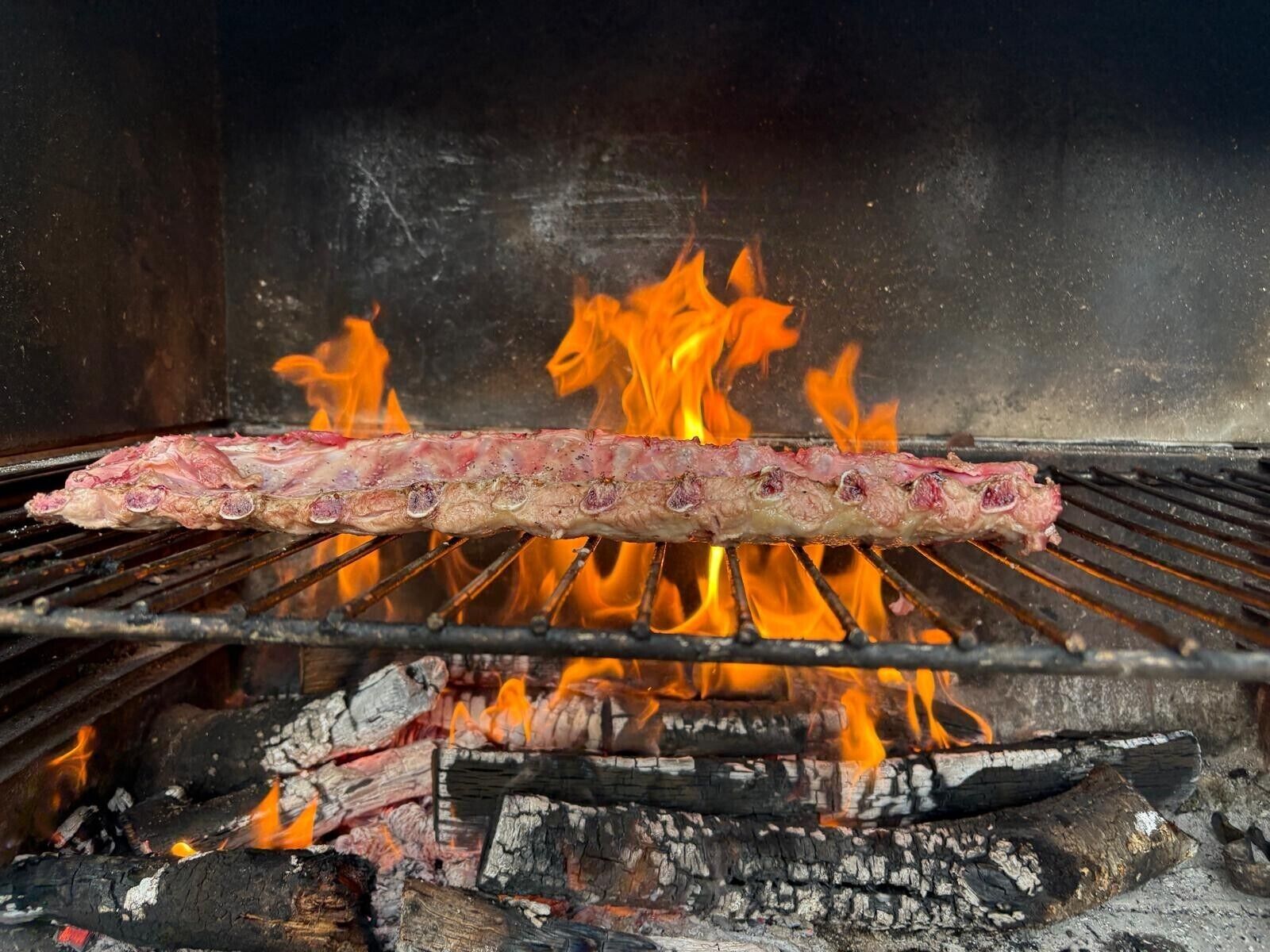 Una parrilla con carne asándose sobre fuego vivo.