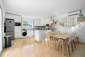 Une cuisine moderne avec des meubles blancs, un îlot central et un coin repas comprenant une table et des chaises en bois.