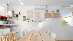 Une cuisine moderne avec des meubles blancs, une table à manger en bois et une vue sur l’extérieur.