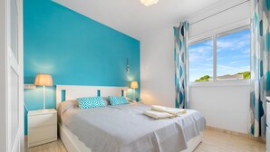 Une chambre à coucher avec un lit, des tables de chevet, une fenêtre avec des rideaux et une vue sur le ciel.