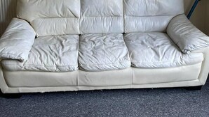 Um sofá de couro branco com um radiador atrás e um quadro acima.