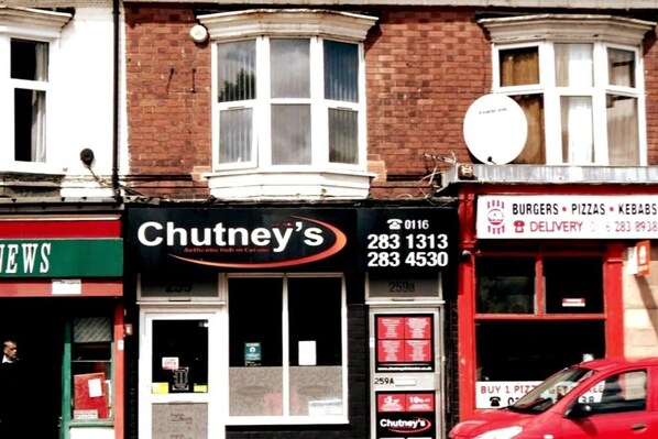 A street view with a restaurant named 'Chutney's' featuring a black signboard with contact numbers.