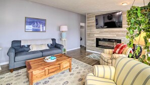 Un salon avec un canapé gris, une table basse en bois, un fauteuil à rayures, un téléviseur fixé à un mur en bois et une cheminée.