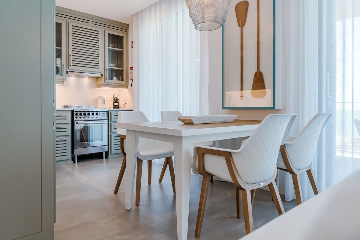 A modern kitchen with white cabinetry, a dining table with chairs, and a pendant light.