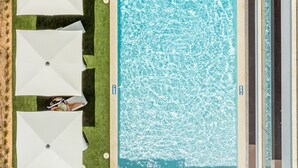 Une piscine sur le toit, agrémentée de plusieurs parasols blancs et de chaises longues, et entourée d’une pelouse bien entretenue.