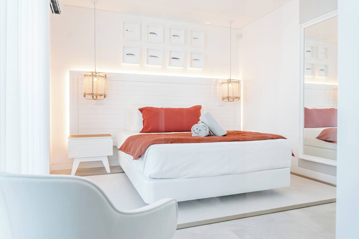 Ein modernes Schlafzimmer mit einem Bett, Nachttischen, einem Sessel und einem großen Spiegel.