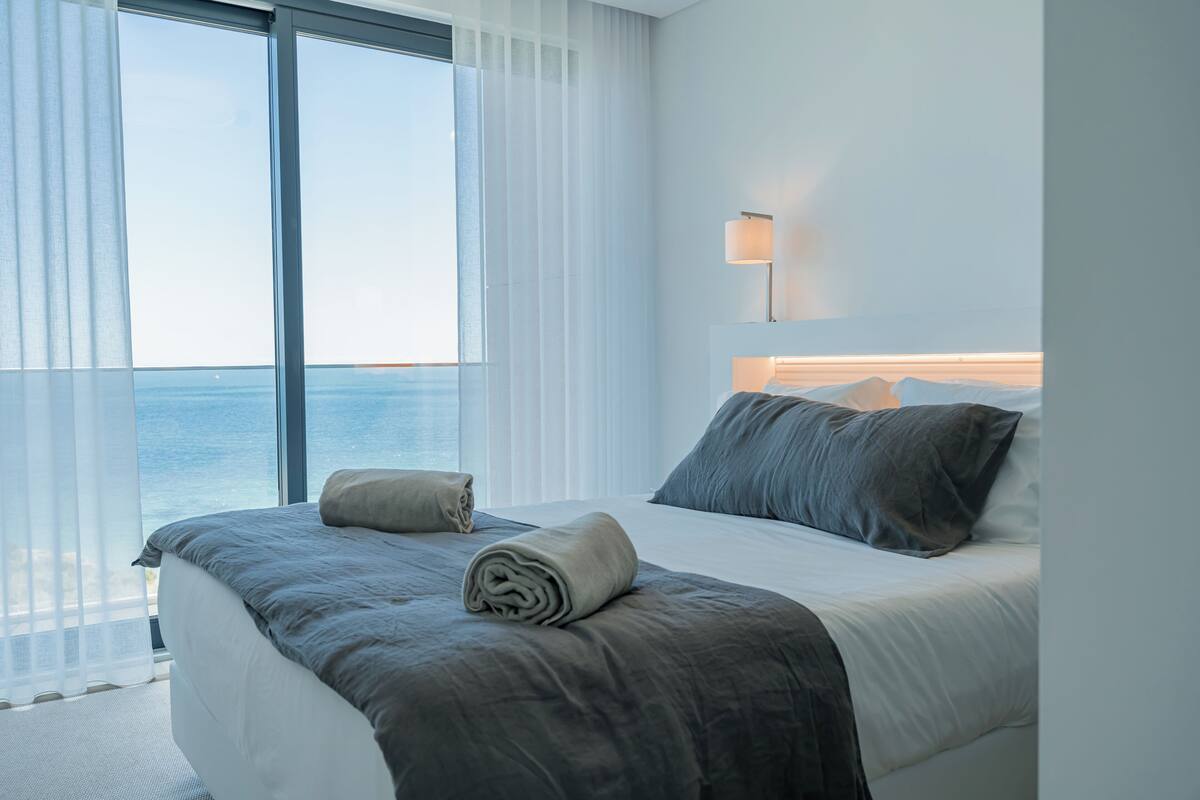 Ein modernes Hotelzimmer mit einem großen Bett, Meerblick und einer Nachttischlampe.