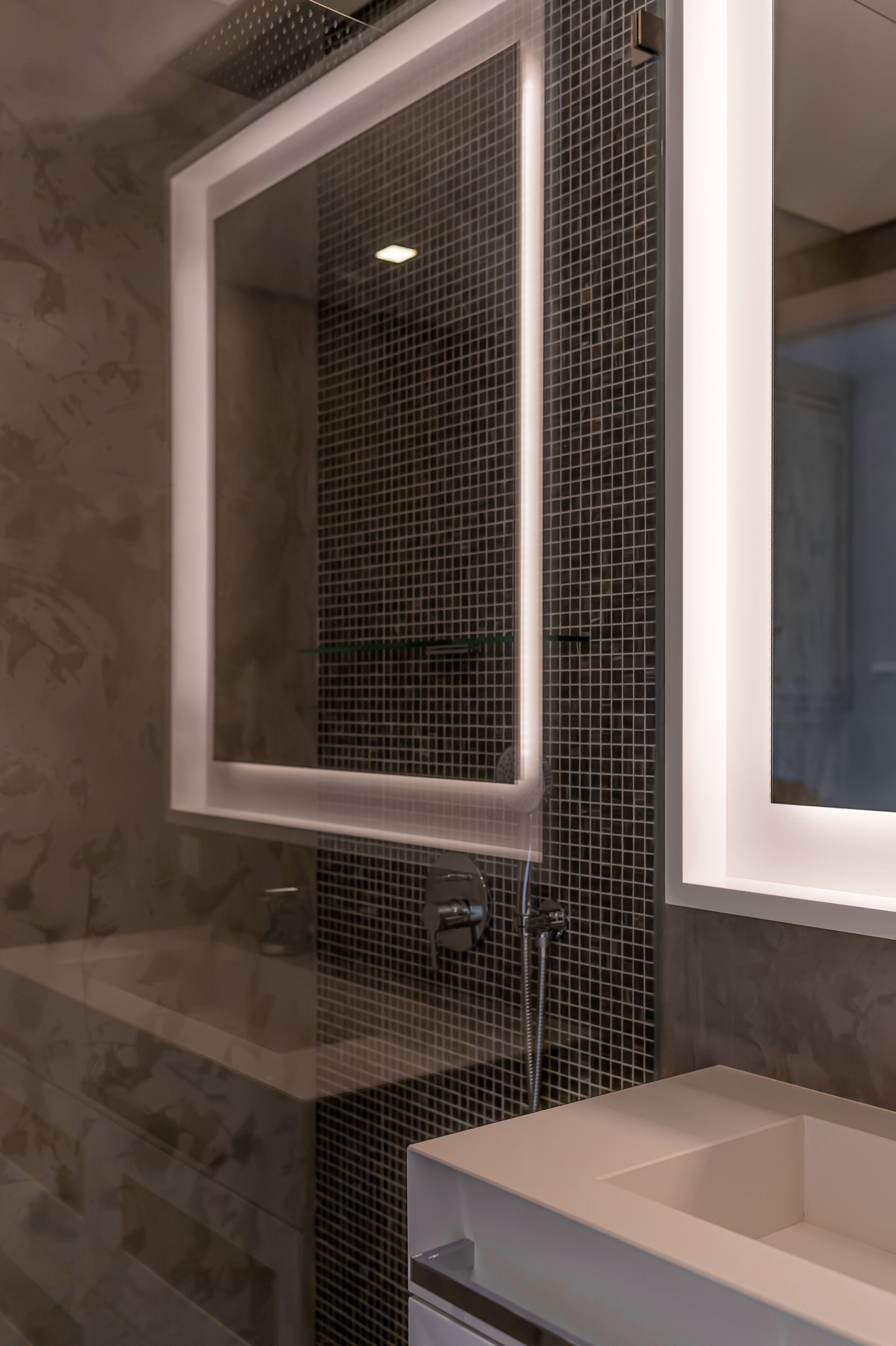 A modern bathroom with a glass-enclosed shower, a white sink, and a tiled wall.