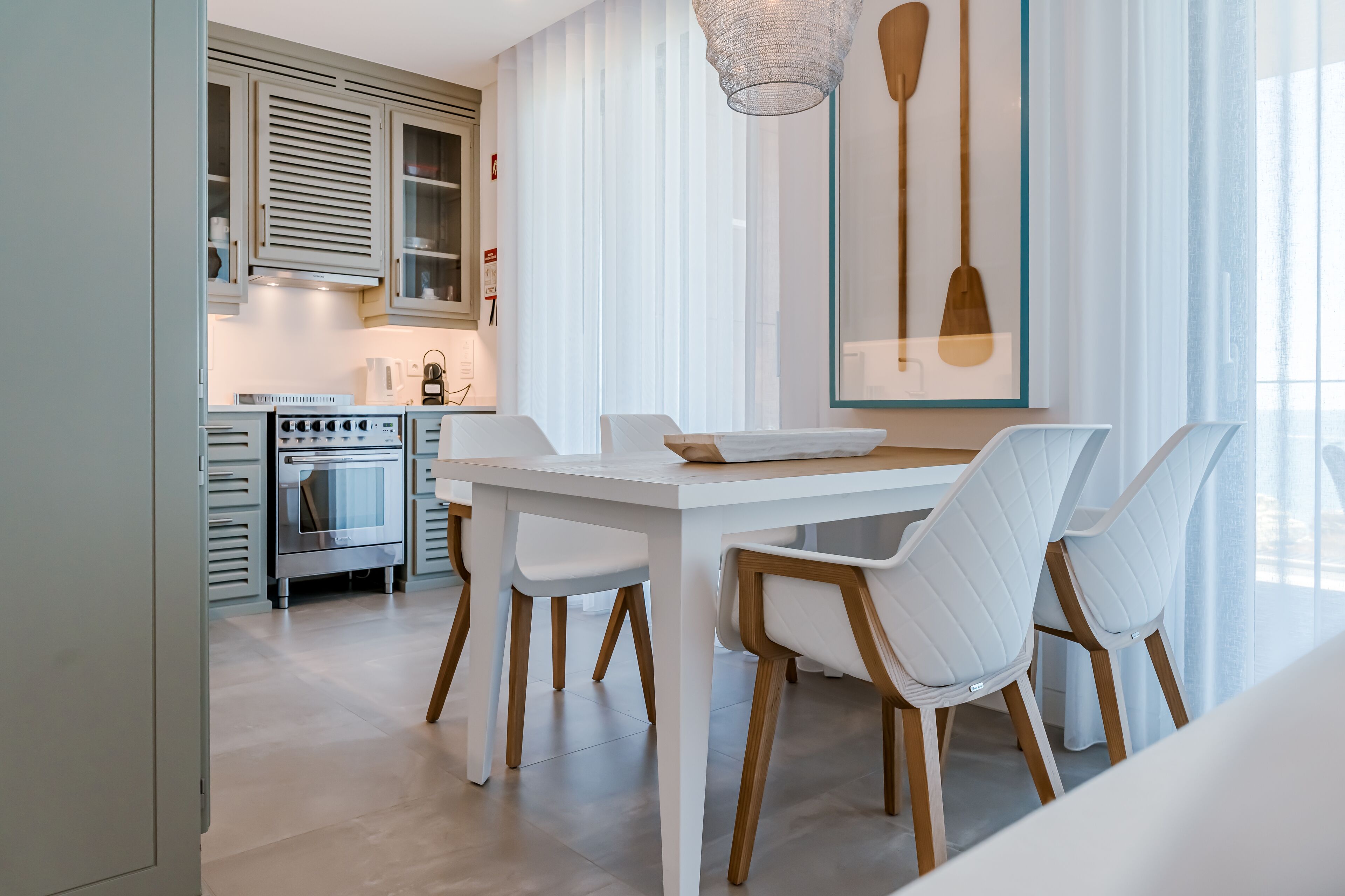 Uma cozinha moderna com armários brancos, uma mesa de jantar com cadeiras e uma luminária pendente.